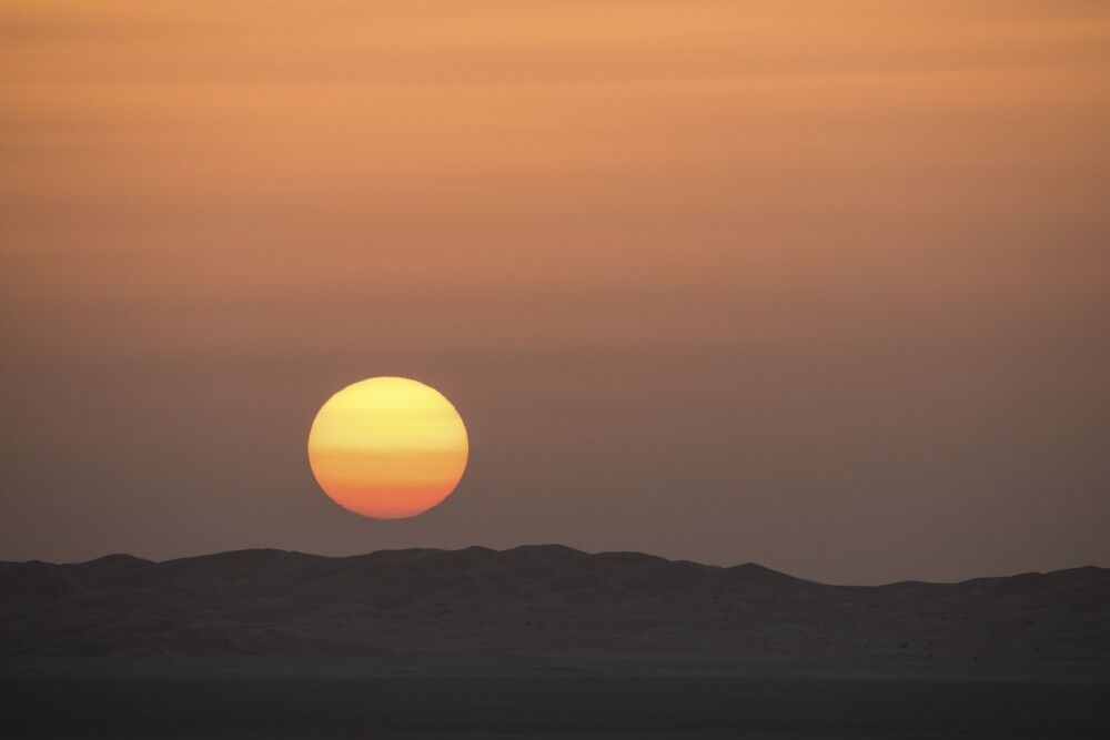 Orangerot verschwindet der Sonnenball hinter den Dünenhängen.