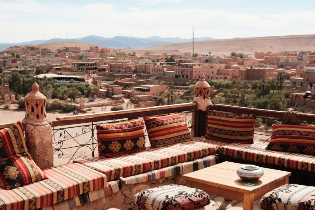 Dachterrasse mit bunten Sitzkissen und Blick über eine Oasenstadt in den Bergen von Marokko