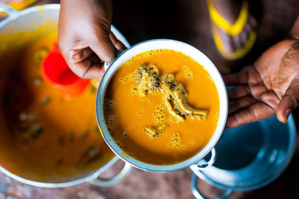 Hände einer kamerunischen Frau, die einen Topf mit traditionellem Taro und „Sauce Jaune“
