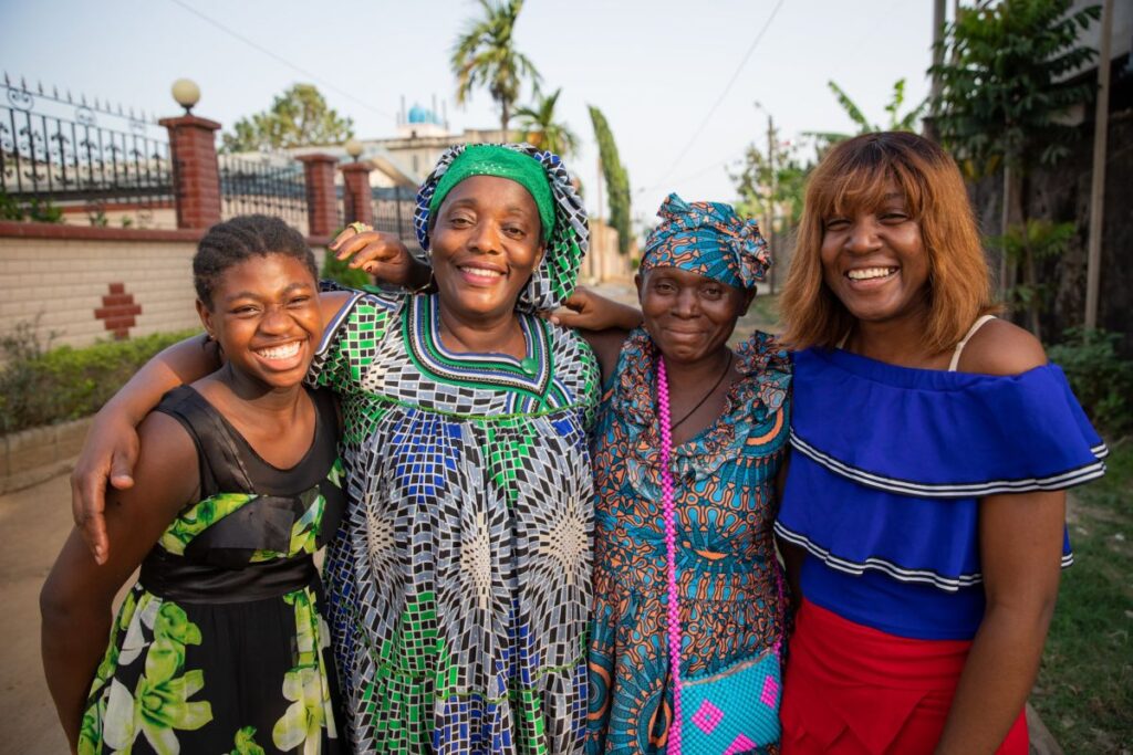 Vier lächelnde Frauen in farbenfroher Kleidung auf einer Straße in Kamerun